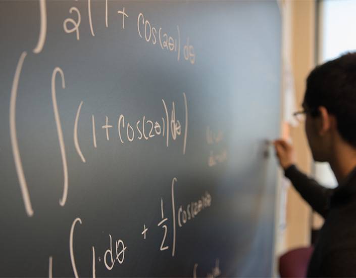 Student writing math formula on blackboard