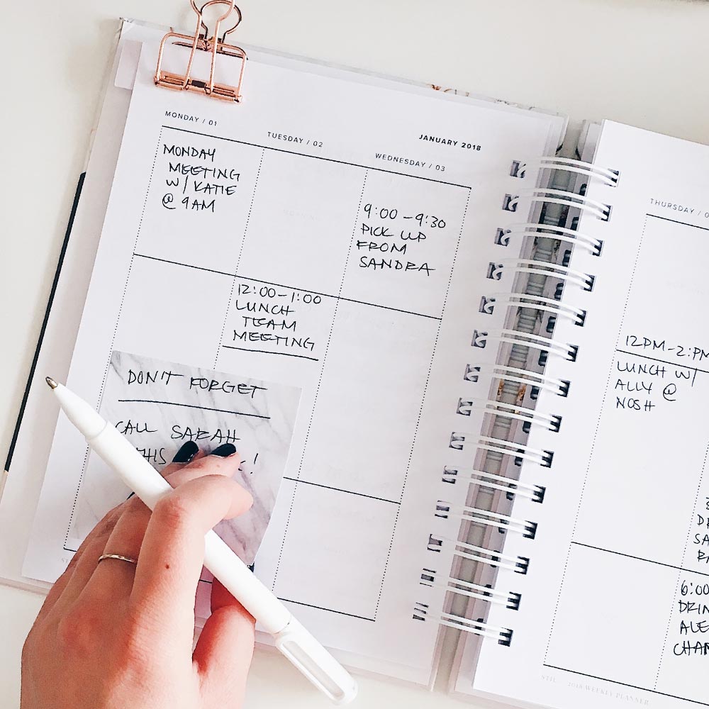 A woman's hand holding a pen marking her calendar.