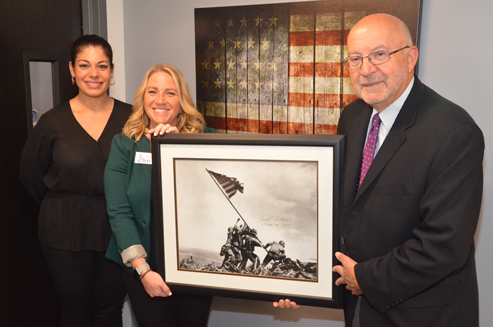 College General Counsel and Marine Corps veteran Louis Petrizzo presents a copy of “Raising the Flag on Iwo Jima,” an iconic photograph of six United States Marines raising the U.S. flag atop Mount Suribachi during the Battle of Iwo Jima in the final stages of the Pacific War during World War II, that is signed by Medal of Honor (MoH) recipient Hershel Williams. Williams was the last living MoH recipient from World War II who died this past July. Williams was awarded the MoH for his heroic actions on Iwo Jima. College Director of Veterans Affairs Shannon O’Neill, center, accepted the framed icon for display in the Veterans Resource Center on the Ammerman Campus in Selden. Elyse Quirk, Veterans Center professional assistant is at left.