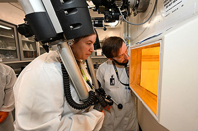 SUNY Suffolk student Arin Morton (left) simulates operating equipment in a hot cell facility — a specialized lab and equipment needed for processing radioactive materials — alongside mentor Michael Chimes of Brookhaven's Isotope Research & Production Department. (Kevin Coughlin/Brookhaven National Laboratory). For a hi-res image of this photo and other photos, visit: https://photos.app.goo.gl/fnZeHU9cnDHkG3yv8